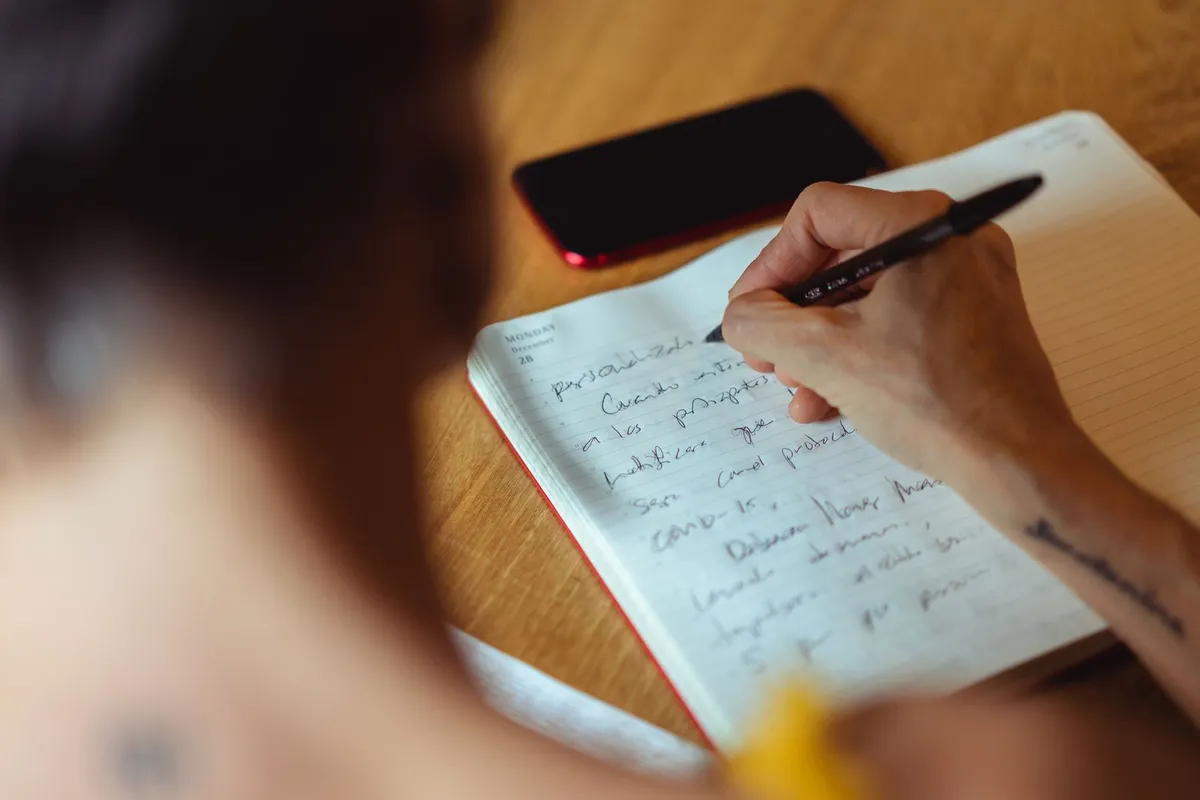 ウッドデスクでノートに筋トレ記録を手書きする手元と、隣に置かれたスマートフォン